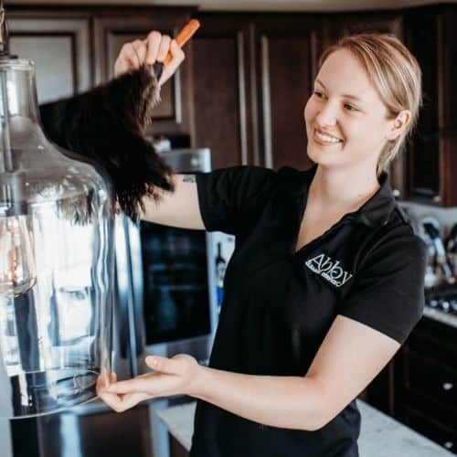 a maid from Abby's Cleaning Service dusting a large glass light fixture